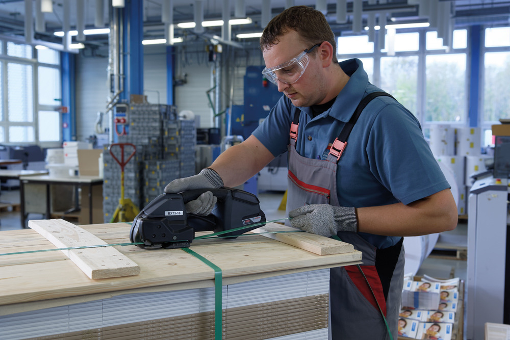 man in safety glasses operating signode bxt3 strapping tool over wood pallets