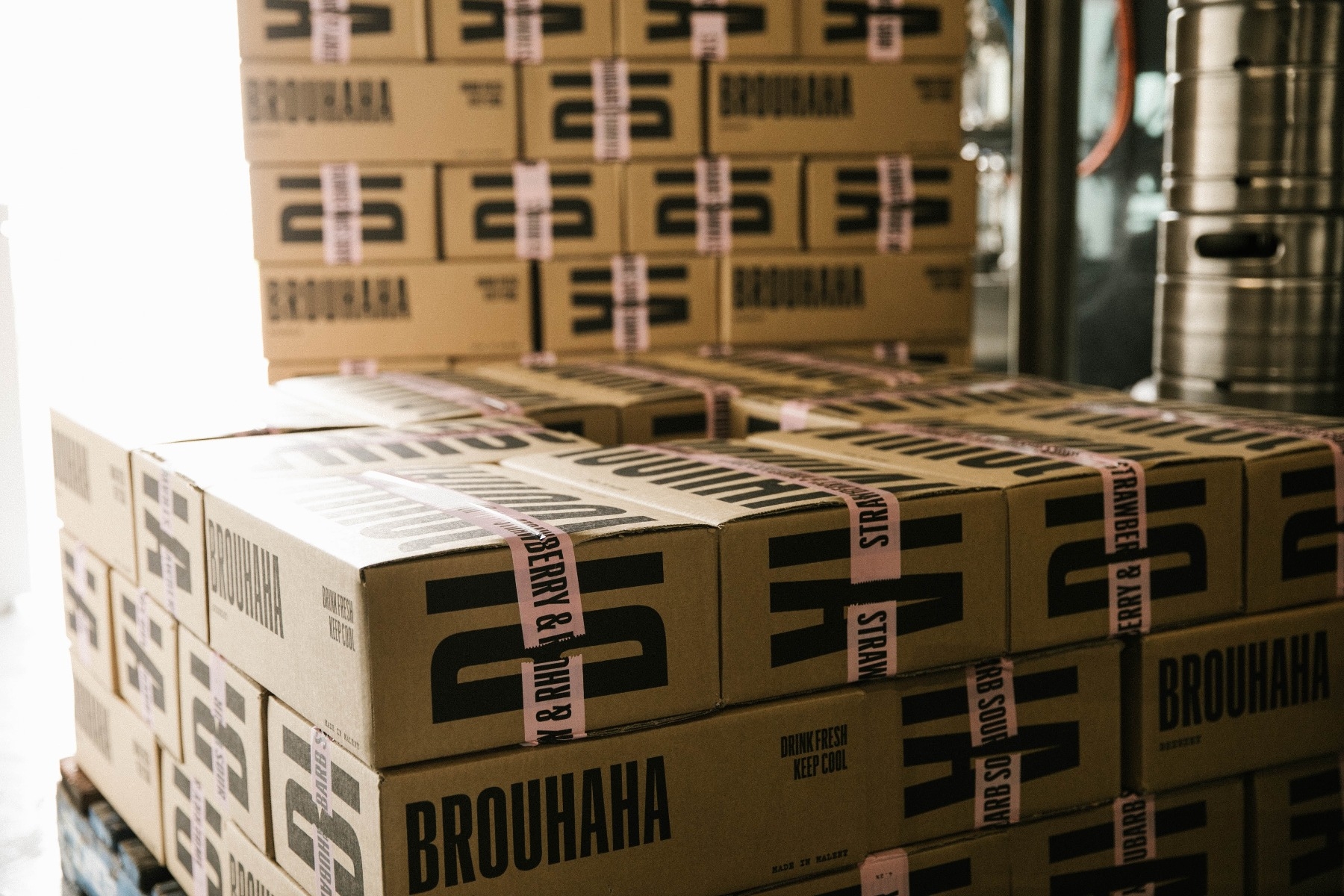 two pallets of stacked brown corrugated boxes each with black brouhaha logo and pink logo printed tape