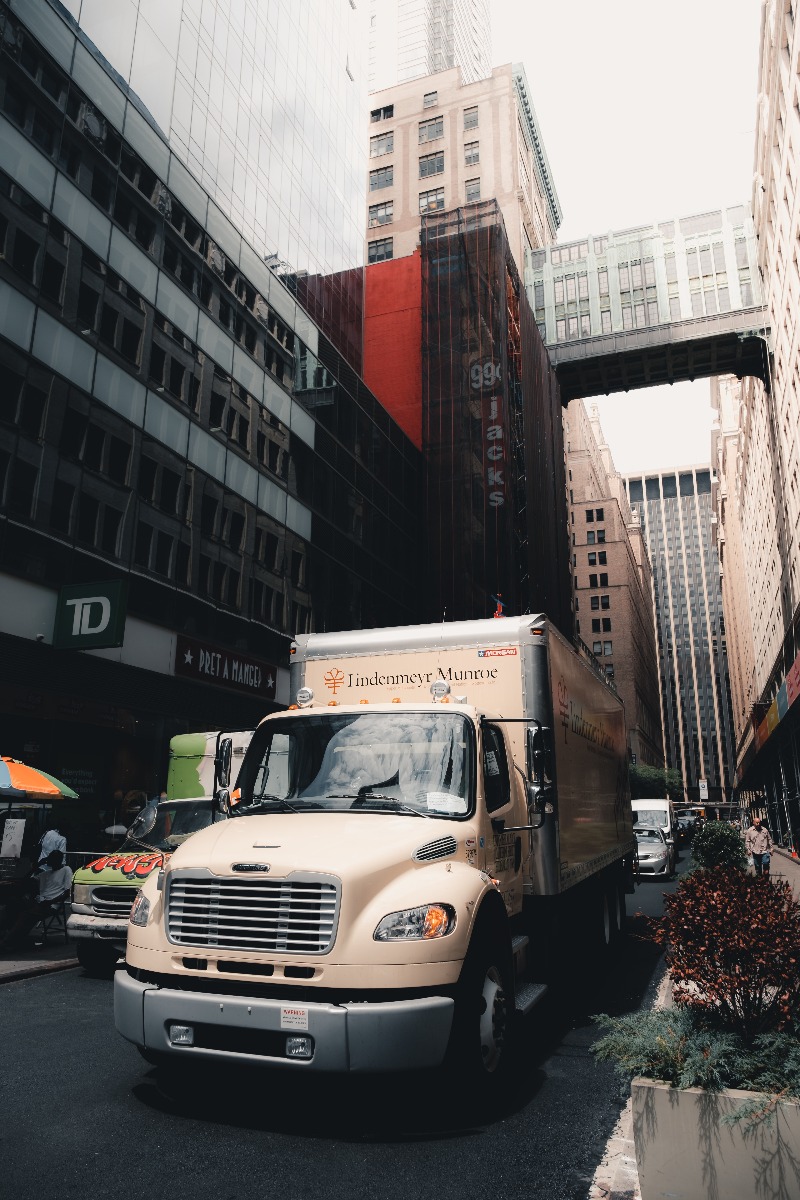 white freight truck driving through narrow city street with tall buildings on either side