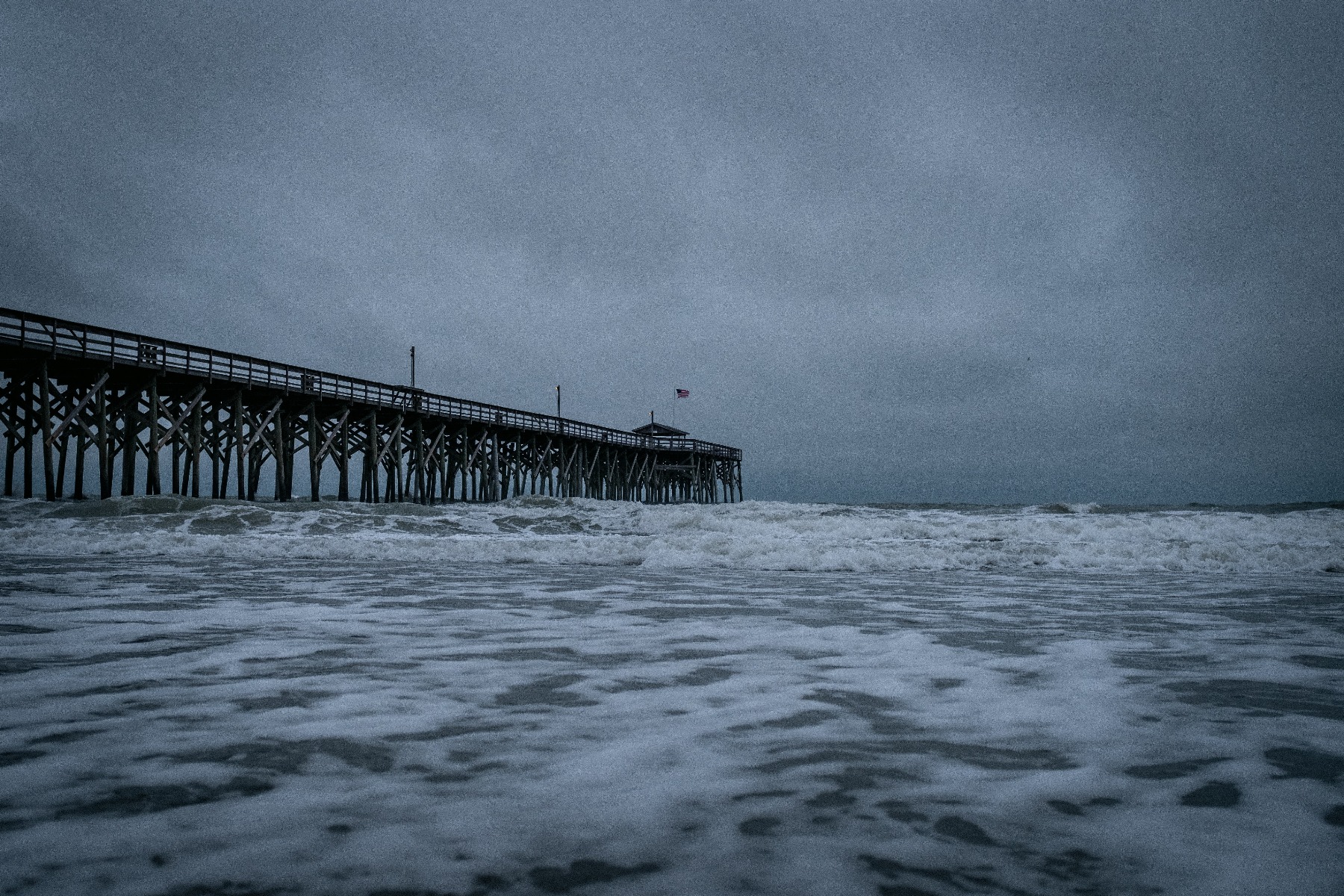 dark stormy sky and sea surrounding long pier extending into ocean