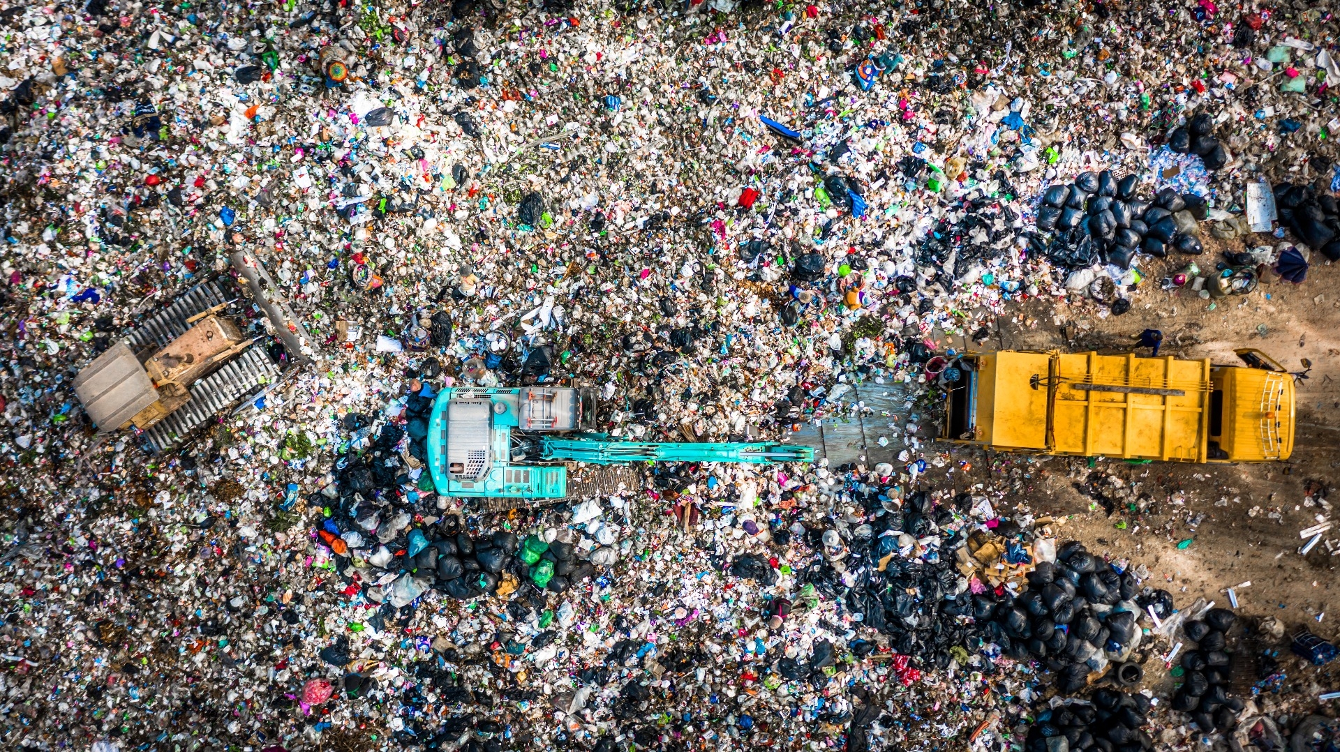 aerial shot of landfill with yellow truck on right, blue truck in middle, and yellow truck on left