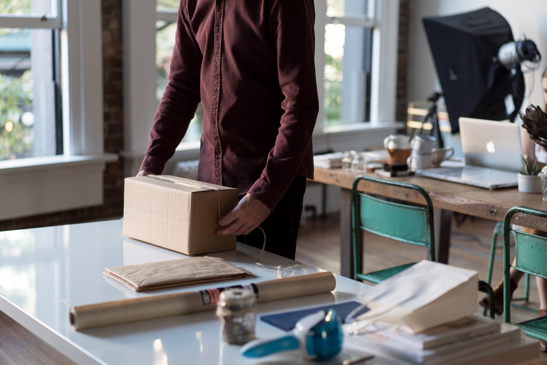 man taping shipping box closed on white workspace with photography equipment in background