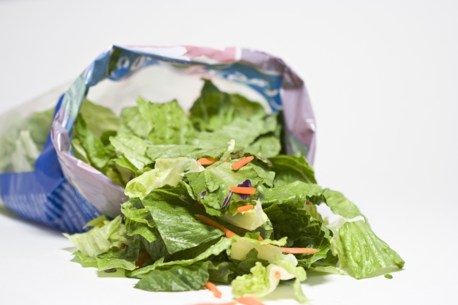 open bag of pre-made salad spilling onto white background