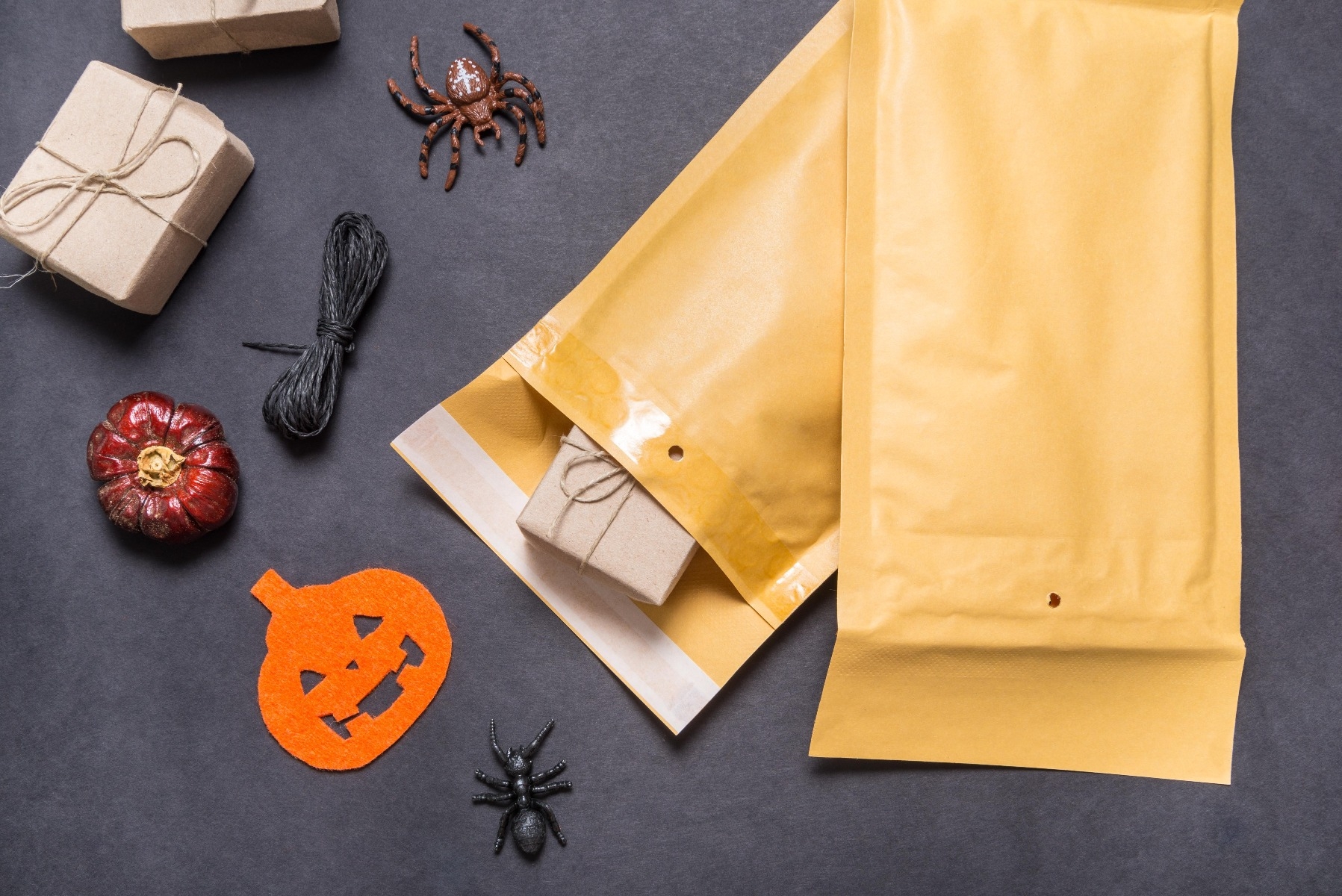 overhead photo yellow padded mailers on right with small box inside and halloween decorations on left all on black table