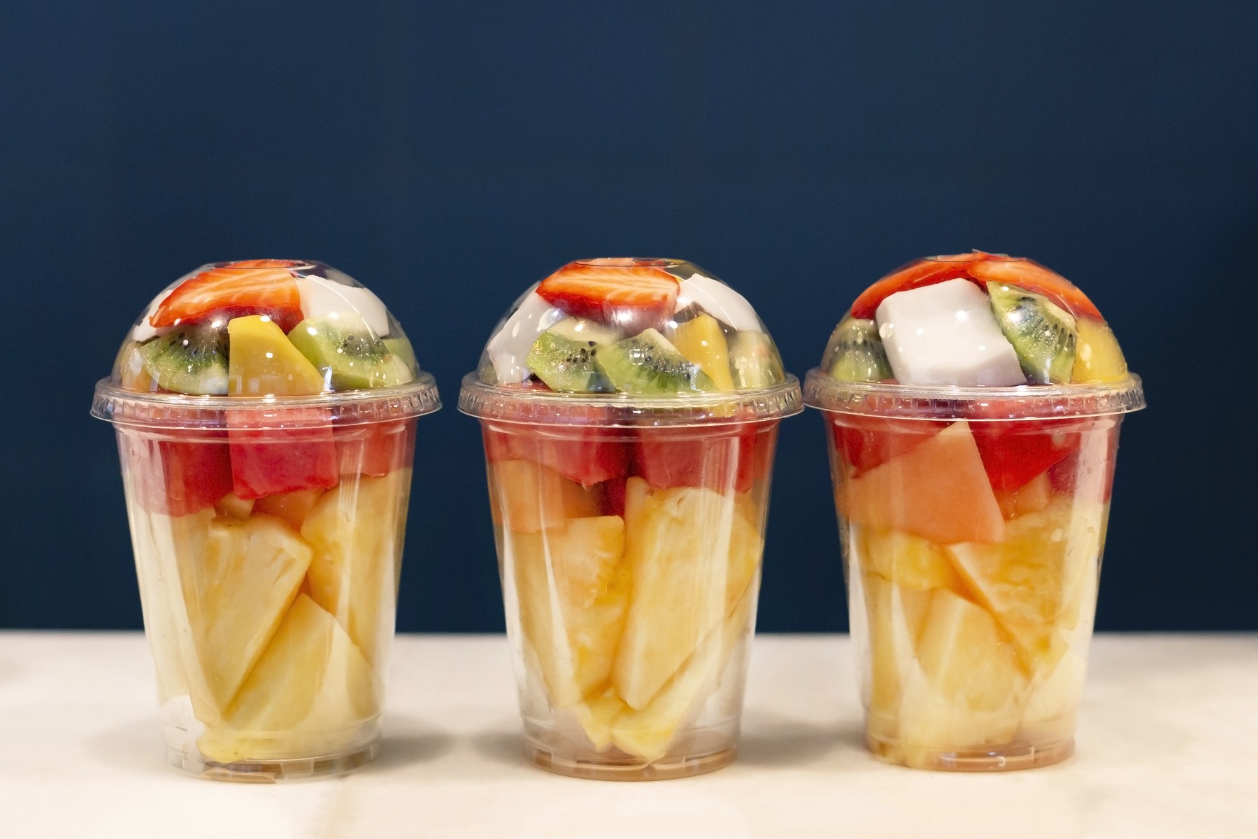 three sets of assorted pre-cut fruits in rigid plastic containers on table