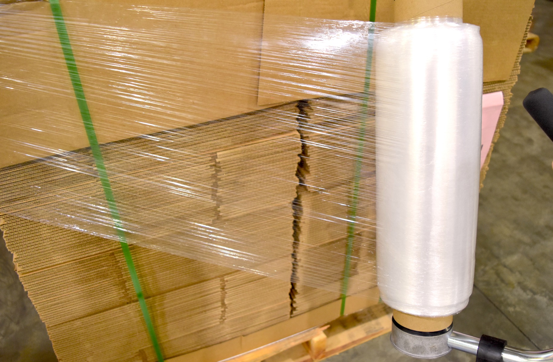 stack of broken down corrugated boxes with two pieces of poly strapping holding them onto pallet and stretch film being applied