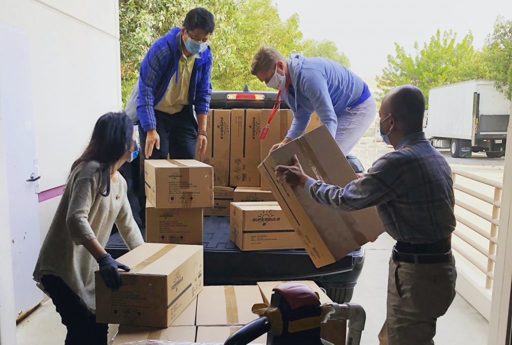 four masked people in a loading bay load taped corrugated boxes onto a pickup truck