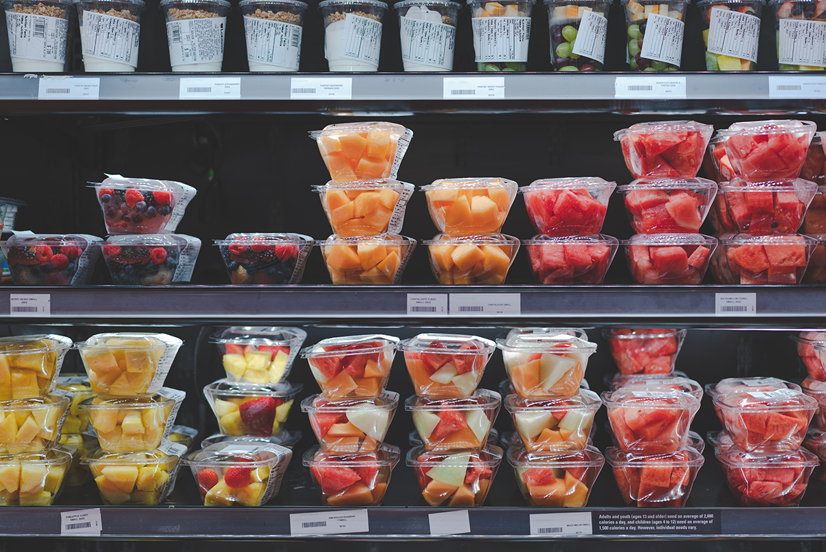 chopped fruits including pineapples and strawberries in plastic clamshell containers lined up on black grocery shelves